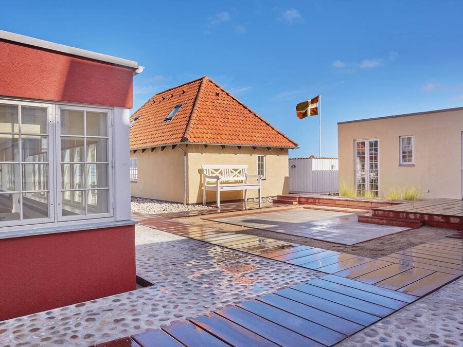 Um imóvel residencial com fachada vermelha, telhado cerâmico e área de pátio com deck de madeira e padrão de pedra.