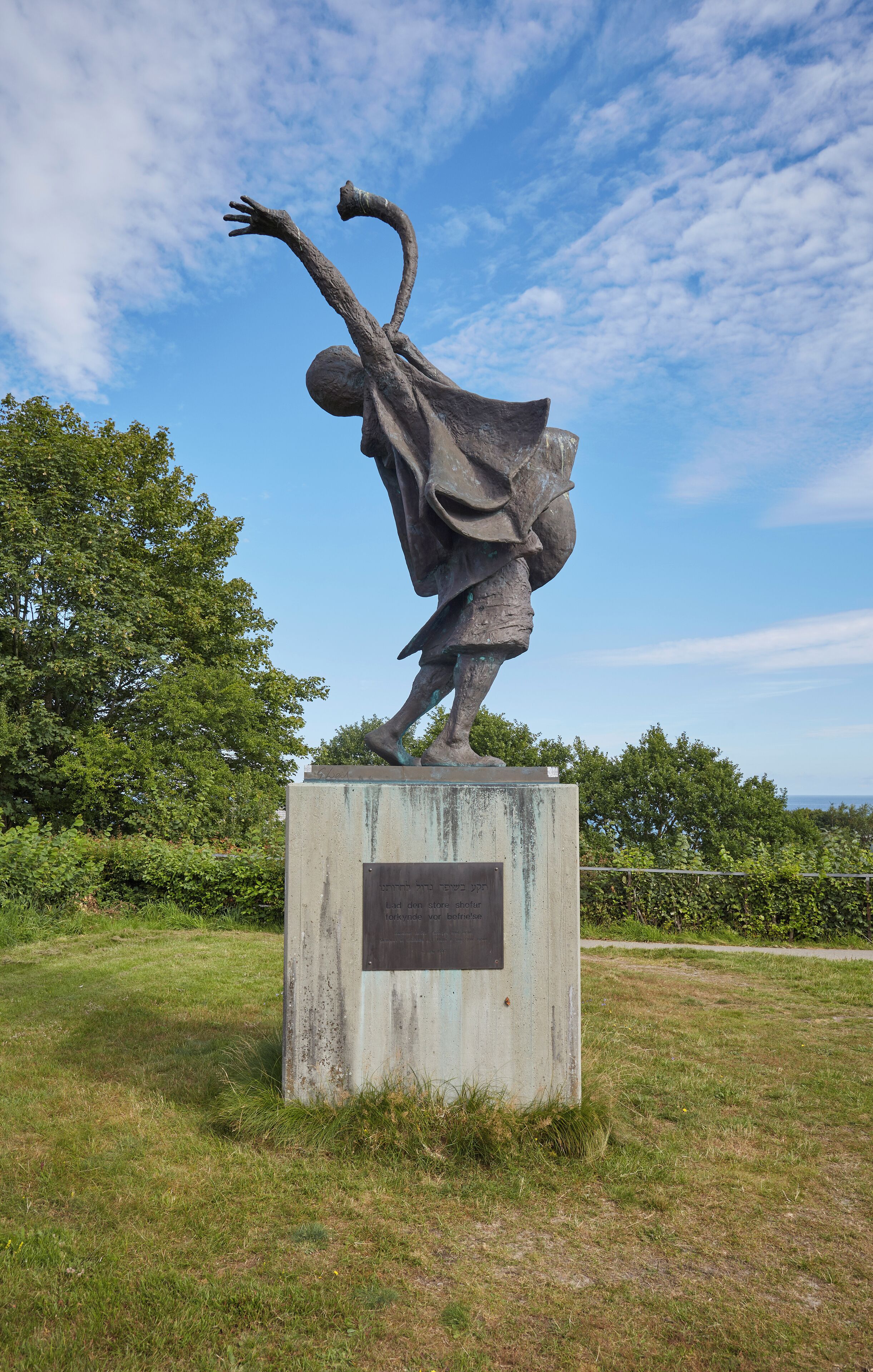 A statue of a person in motion, set in a grassy area with trees and a clear sky in the background.