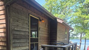 A wooden cabin with a deck, a door, and a view of a lake. - Waterfront cabin on Long Lake. (New Auburn)