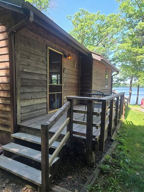A wooden cabin with a deck, a door, and a view of a lake.