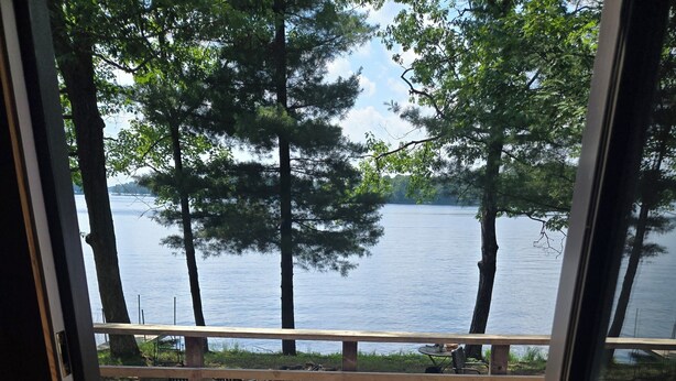 A wooden deck with a railing overlooking a lake, surrounded by trees. - Waterfront cabin on Long Lake. (New Auburn)