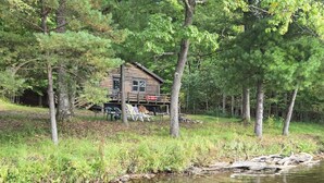 A cabin by a clear stream surrounded by trees. - Waterfront cabin on Long Lake. (New Auburn)