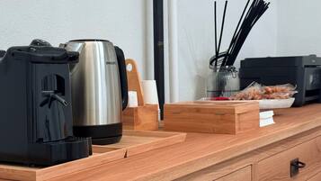 Un bancone di legno con una macchina da caffè, un oggetto cilindrico nero, un oggetto cilindrico bianco, una scatola di legno con un manico, una stampante nera e un barattolo di vetro con bastoncini neri.