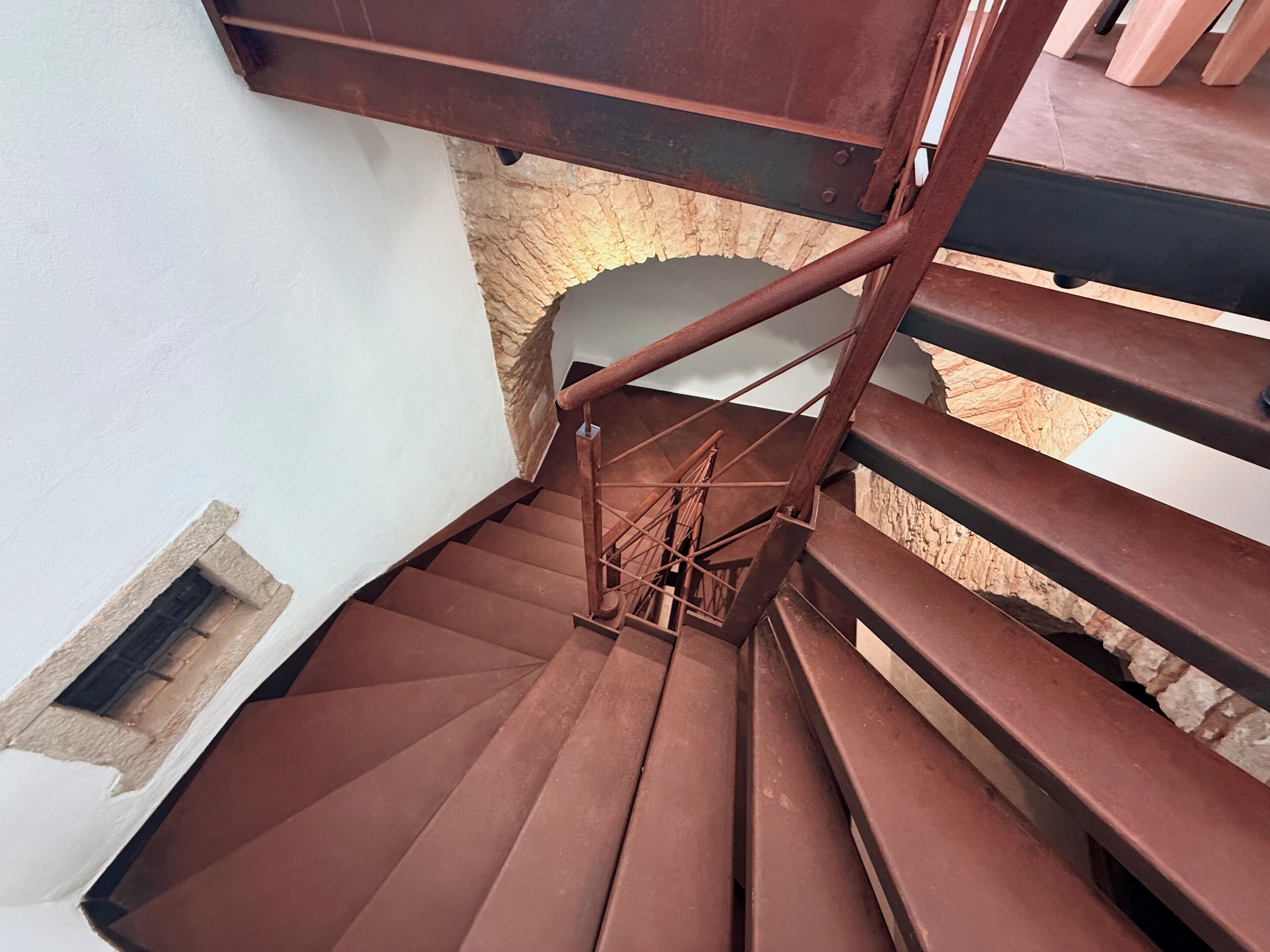 A spiral staircase with a metal railing, leading to a stone archway.
