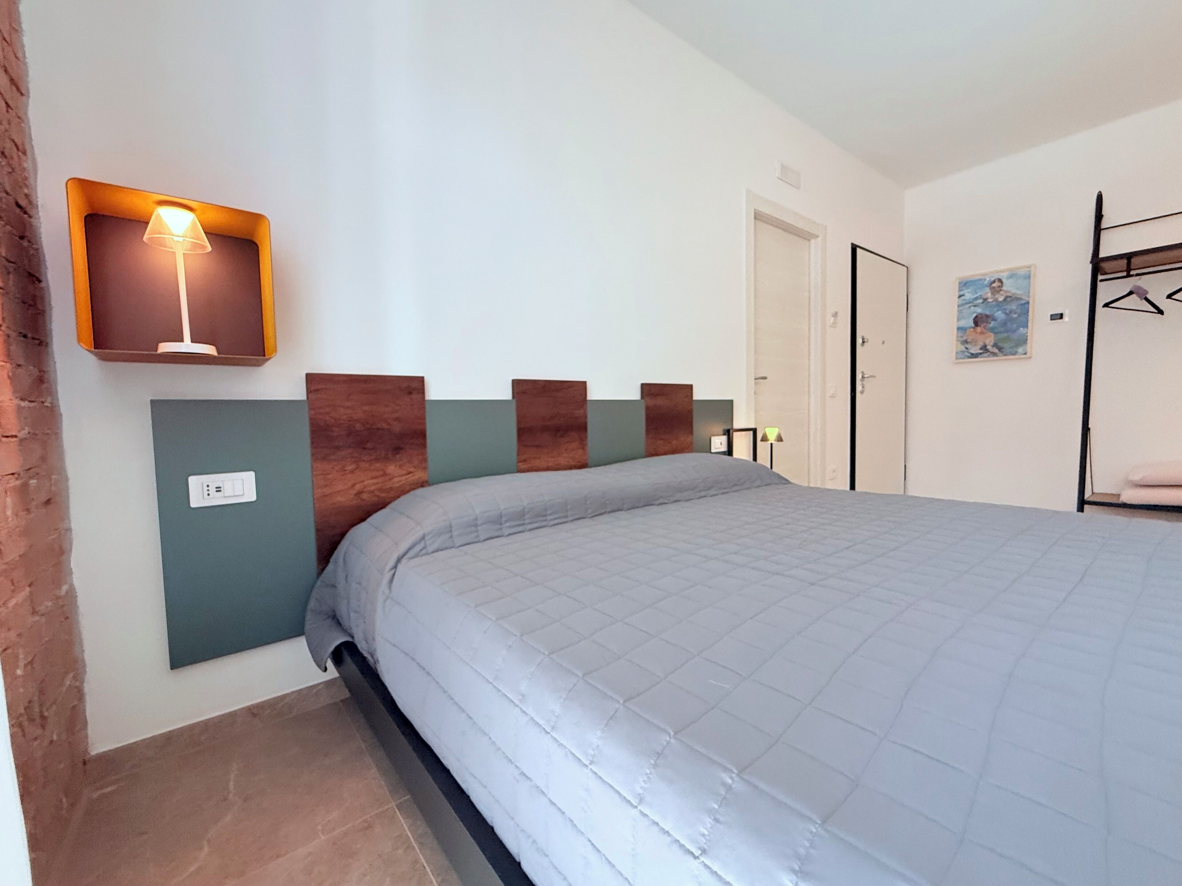 Une chambre à coucher avec un lit, une lampe fixée au mur, une porte et un tableau.