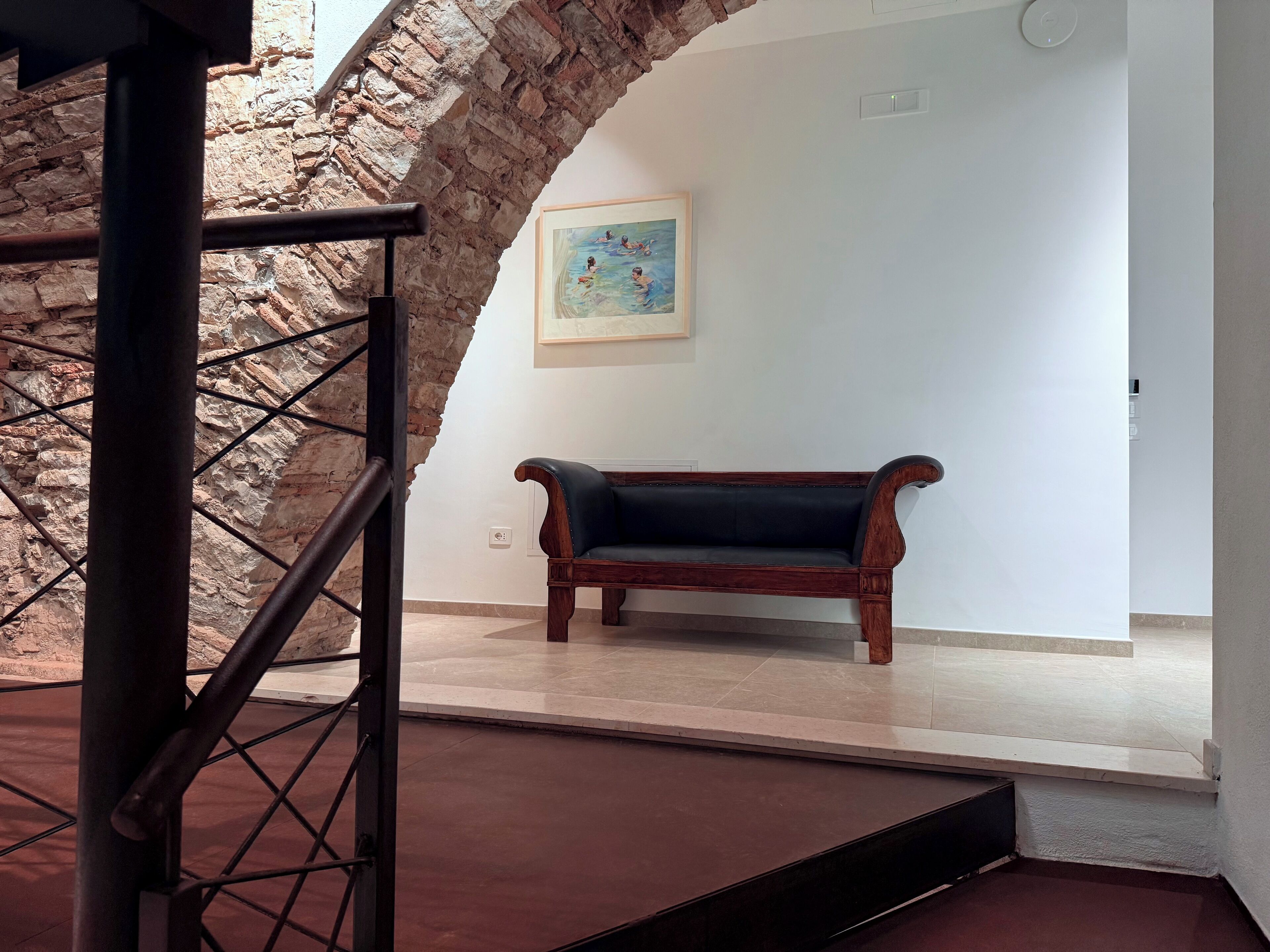 A staircase with a stone wall, a wooden bench, and a framed painting on the wall.