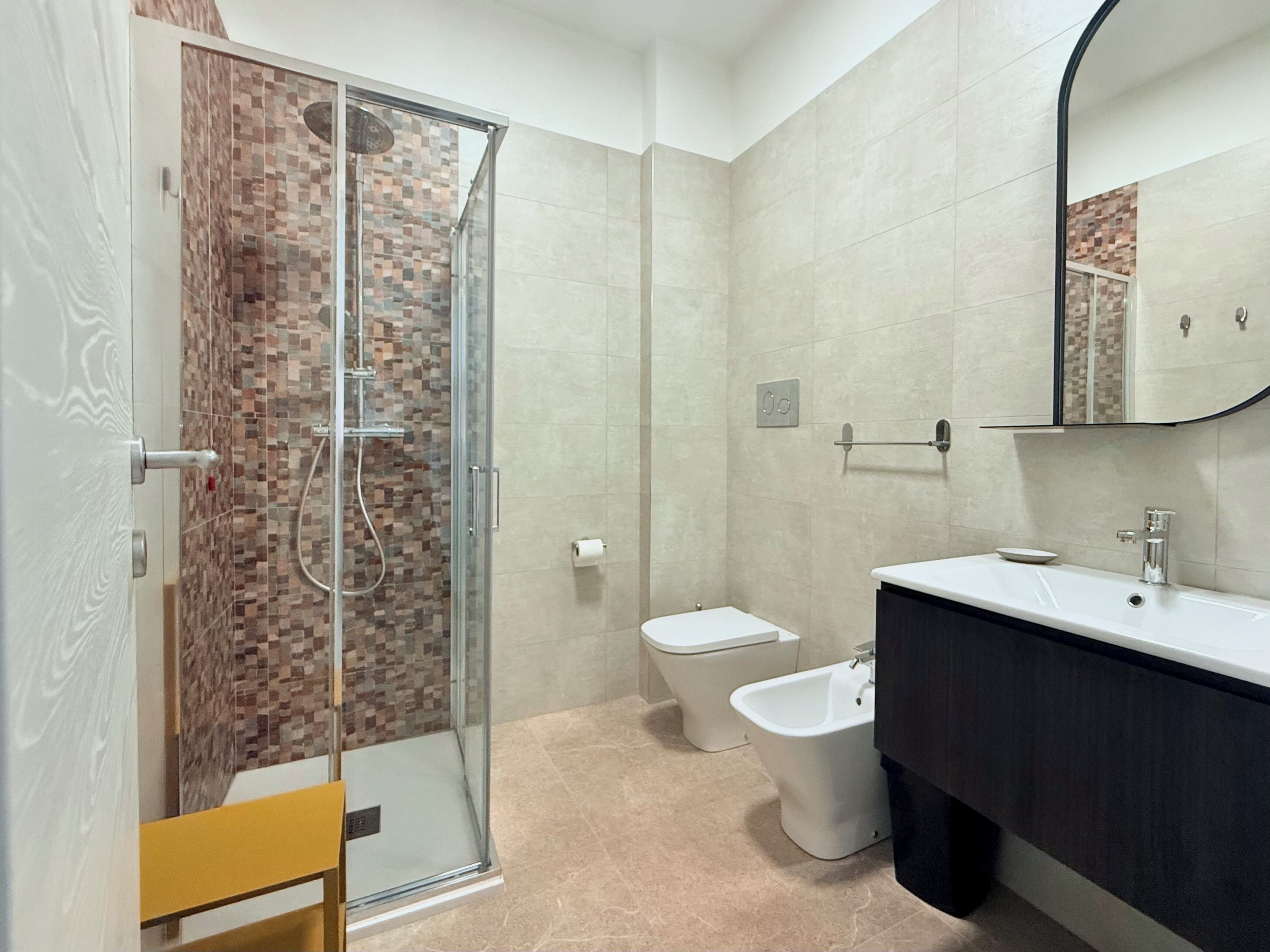 Un baño moderno con cabina de ducha de vidrio, inodoro, bidé y tocador con espejo.