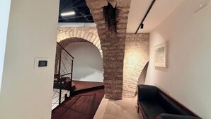 Ein Zimmer mit einem Steingewölbe, einem schwarzen Ledersofa und einer Treppe mit Metallgitter.