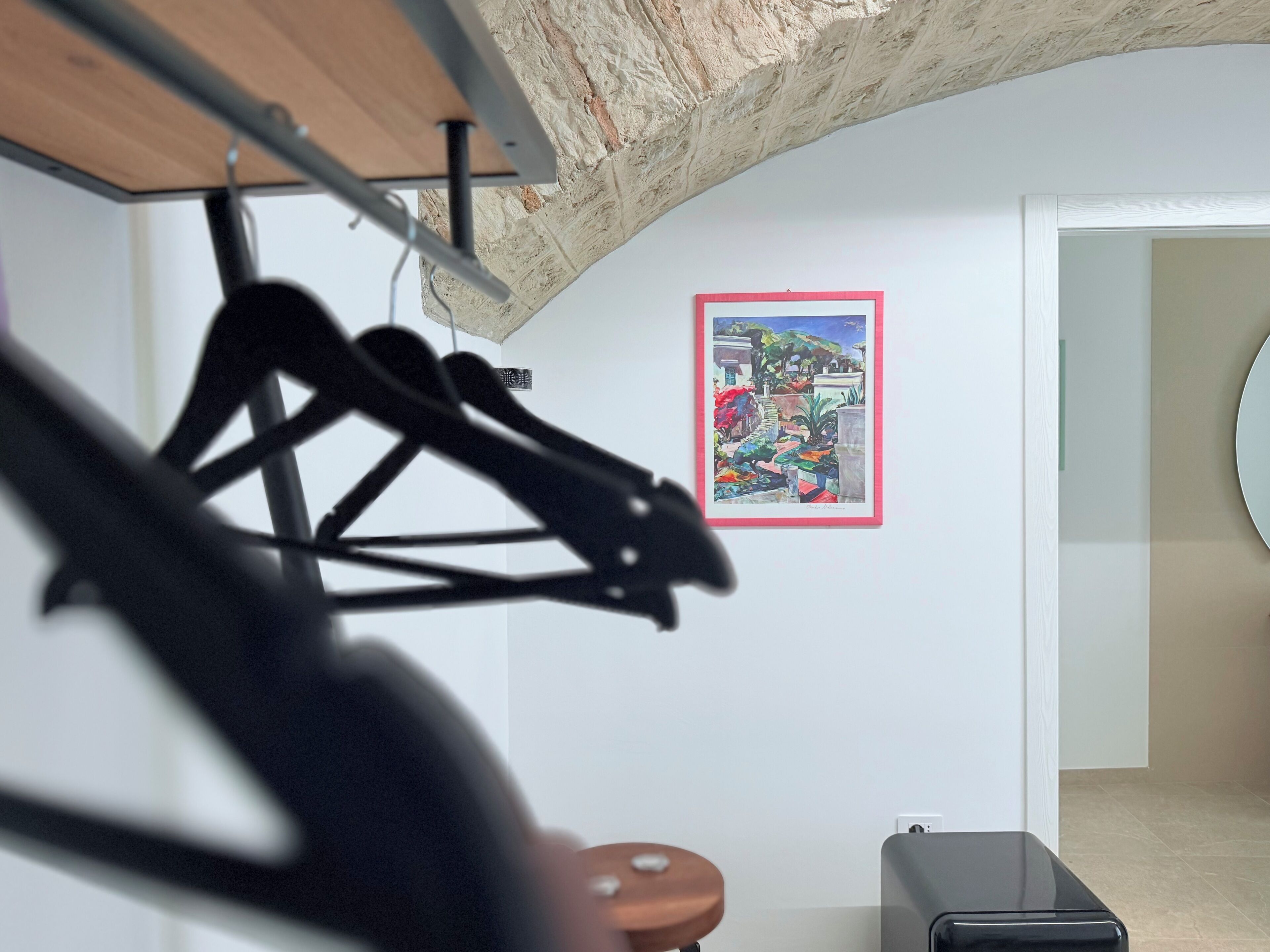 A room with a wooden ceiling, a black chair, a table, a framed painting on the wall, and a door leading to another room.