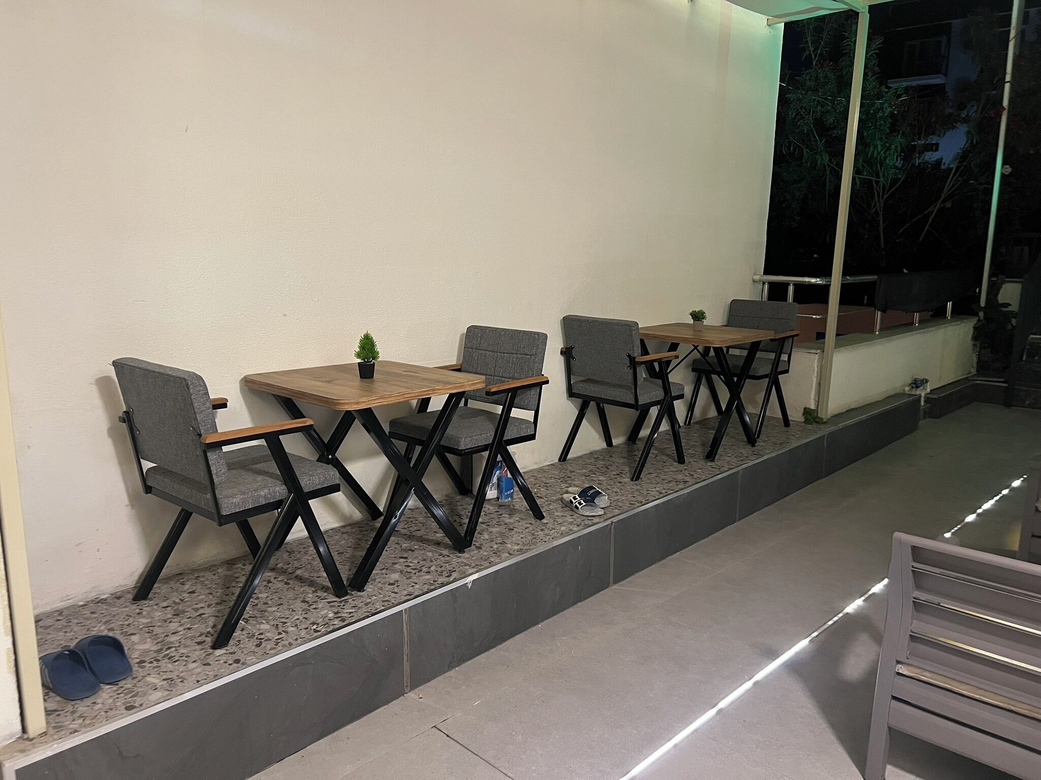 A seating area with tables and chairs, a small plant on one table, and a window with a view of trees.