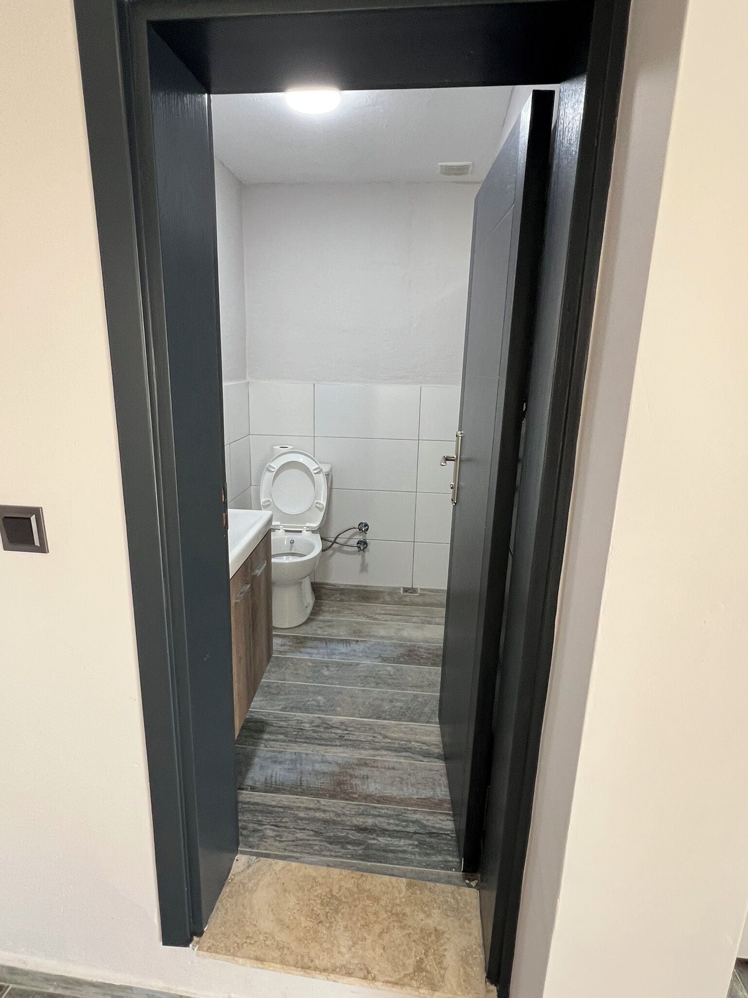 Un pasillo estrecho que conduce a un baño con inodoro, lavamanos y paredes con azulejos.