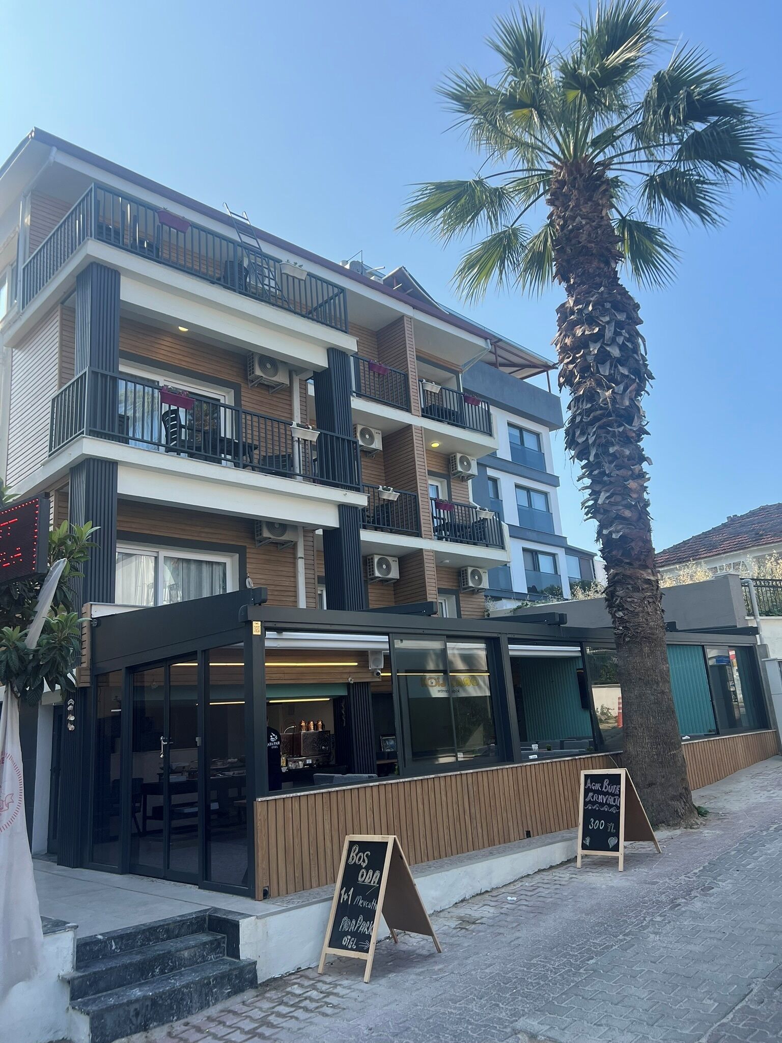 A multi-story building with balconies, a palm tree, and a signboard.