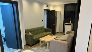 A modern living room with a sofa, a coffee table, and a bed with a neatly folded towel. - Ada Park Otel (Kusadasi)