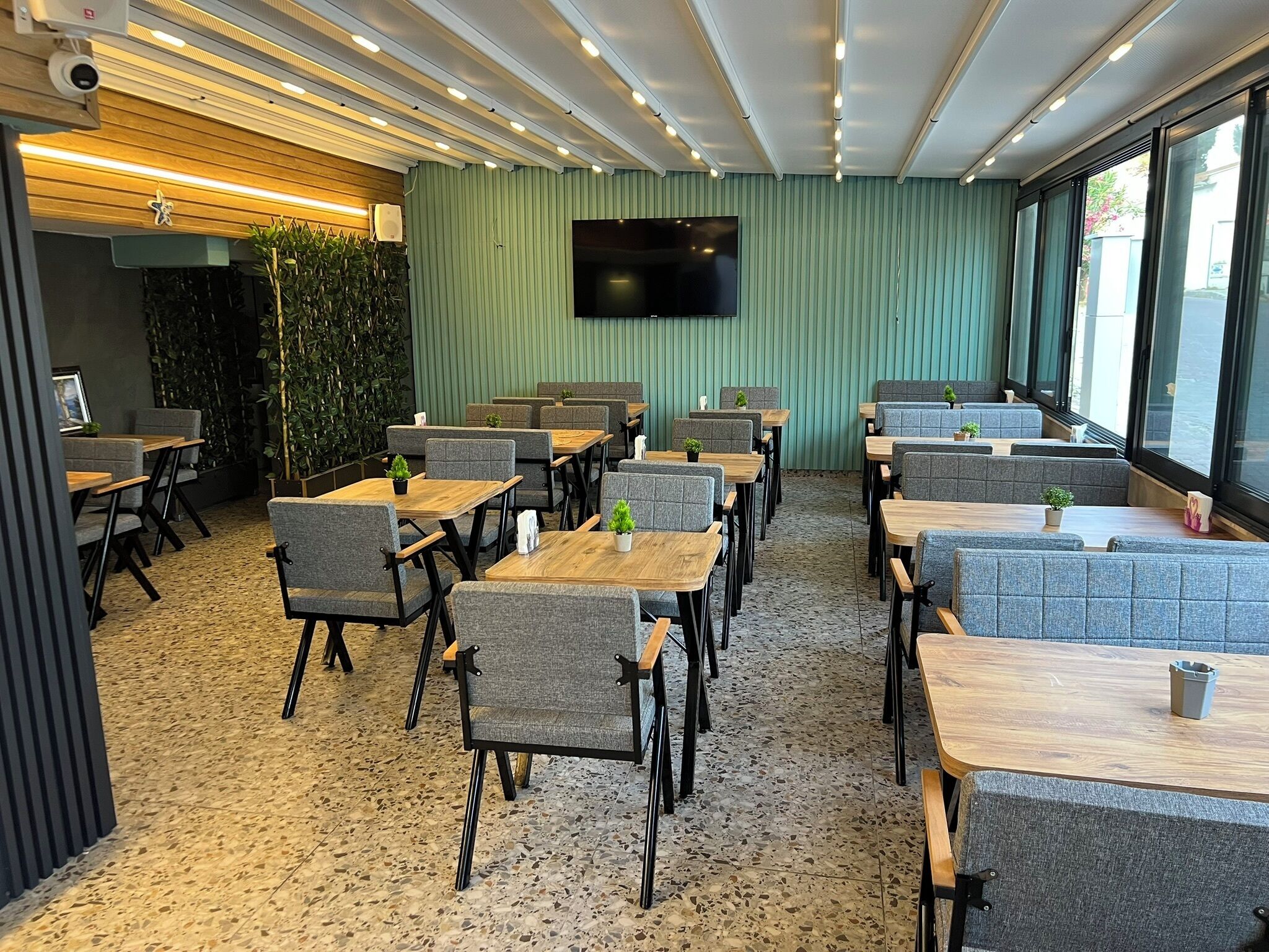Un restaurante moderno con cabinas y mesas, un televisor de pantalla plana y una pared verde con plantas.