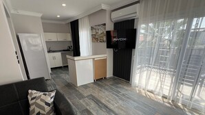 A modern living area with a sofa, a TV, a kitchen, and a balcony with curtains. - Ada Park Otel (Kusadasi)