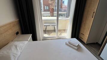A hotel room with a bed, a wooden headboard, a wardrobe, and a sliding glass door leading to an outdoor balcony.