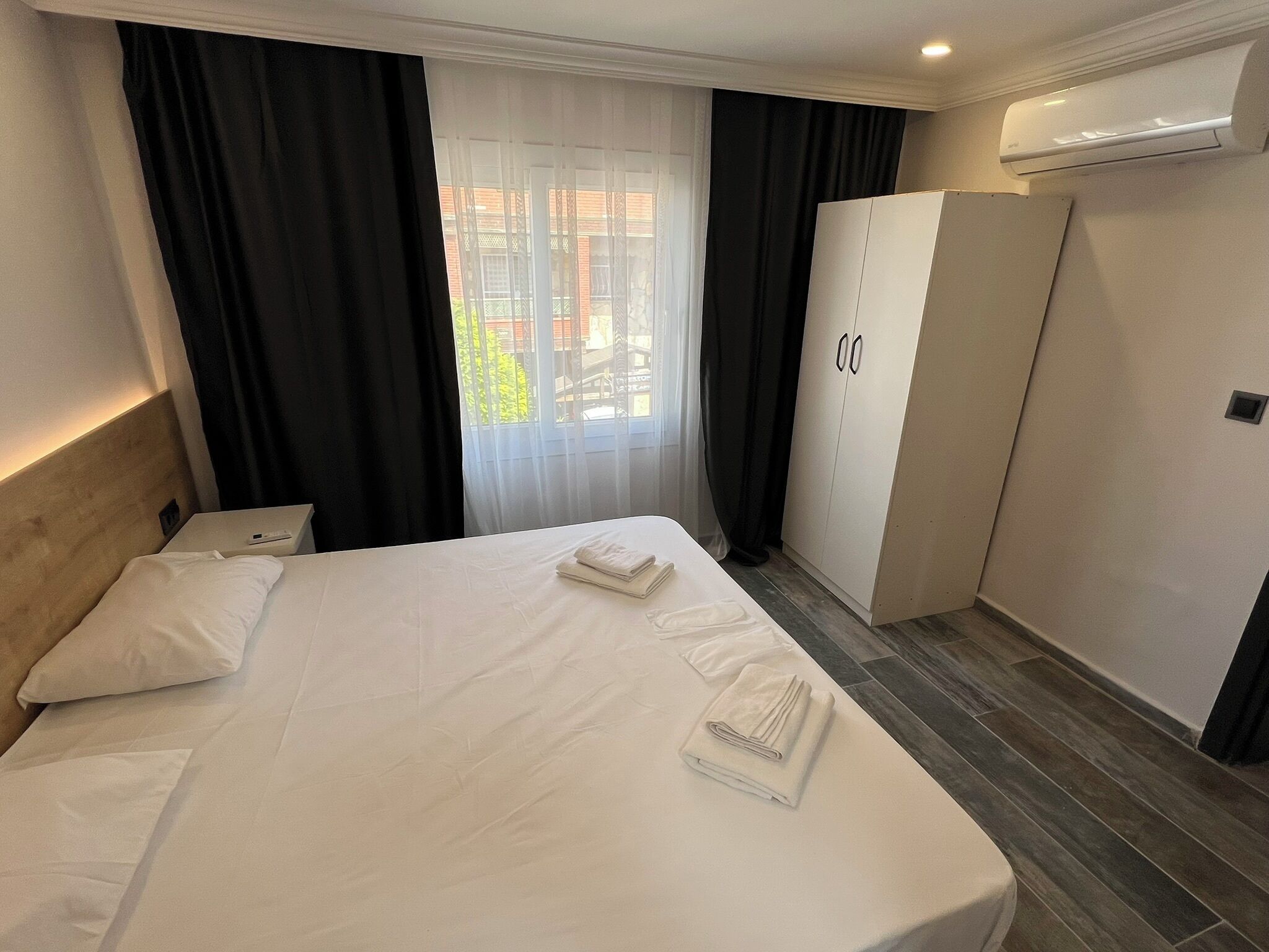 A hotel room with a bed, a nightstand, a wardrobe, and a window with curtains.