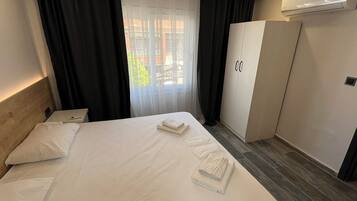 Una habitación de hotel con cama, mesita de noche, armario y ventana con cortinas.