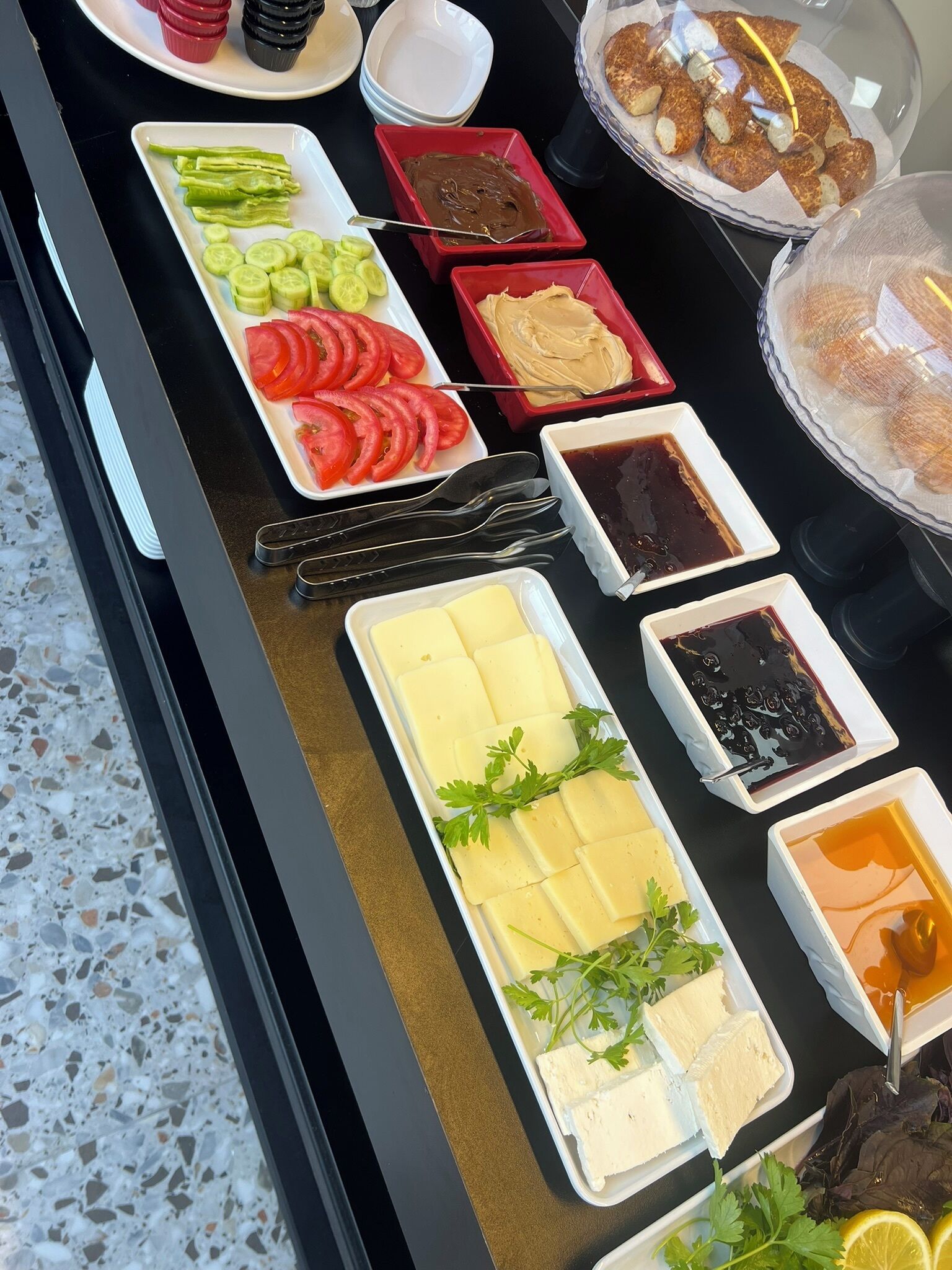 A buffet with various food items including sliced cucumbers, tomatoes, cheese, and different sauces.