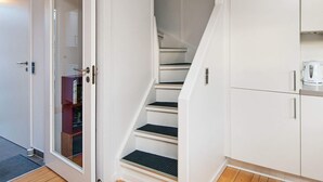 Un escalier aux murs blancs et au plancher en bois, menant à un palier où se trouvent une armoire blanche et une bouilloire.