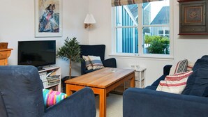 Un salon équipé d’un téléviseur, d’un canapé, d’une table et d’une fenêtre donnant sur des immeubles.