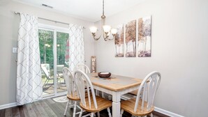 A dining area with a wooden table, white chairs, a chandelier, and artwork on the wall.