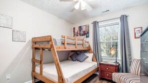 A bunk bed room with a ceiling fan, a window with blinds, a small table, and a chair.