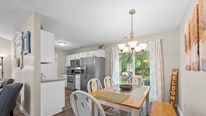 A modern kitchen with white cabinets, a central island, and a dining area with a wooden table and chairs.