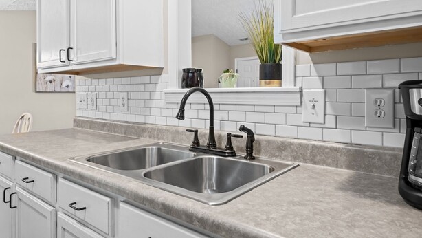 A modern kitchen with white cabinetry, a double sink, and a countertop.