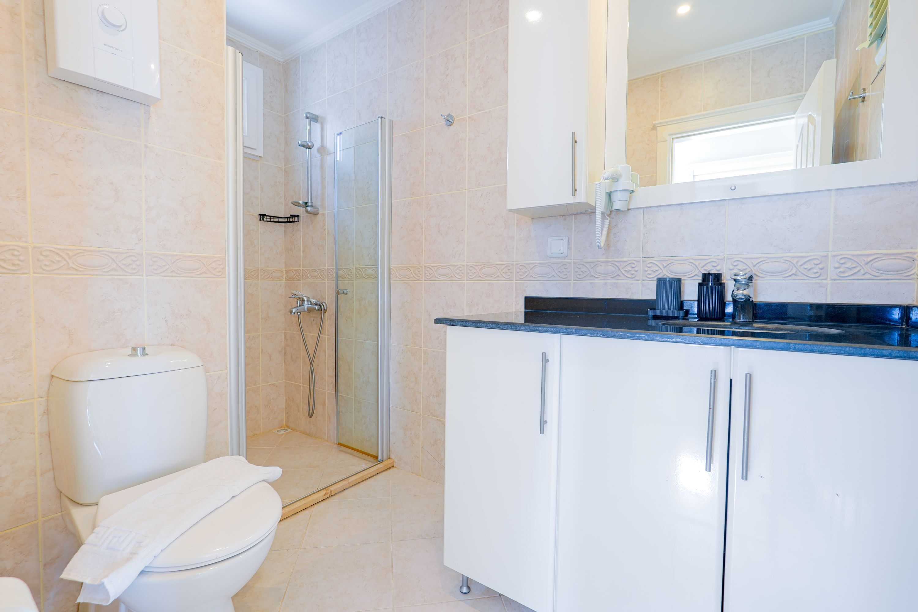 Un baño con inodoro, ducha y armarios blancos.