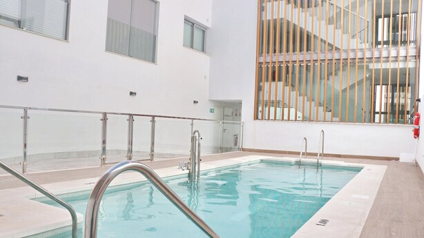 An indoor swimming pool with a glass railing, a tiled floor, and a staircase in the background. - Apartamento Terrazas de Conil (conil de la frontera)