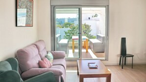 A living room with a sofa, a coffee table, and a sliding glass door leading to an outdoor patio with a table and chairs. - Apartamento Terrazas de Conil (conil de la frontera)