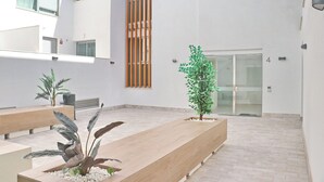 A modern indoor courtyard with a wooden bench, potted plants, and a glass door entrance. - Apartamento Terrazas de Conil (conil de la frontera)