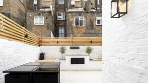 A courtyard with a black table, two potted plants, and a white brick wall. - GuestReady – Stylish 3bed in Central Pimlico (London)