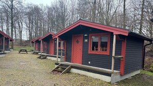 Een rij blokhutten met rode accenten en zwarte bekleding, genummerd 48 en 47, met een klein terras en een picknicktafel.