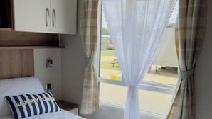 Un dormitorio con cama, mesita de noche, armario y ventana con cortinas.
