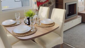 Un comedor con una mesa dispuesta para cuatro, un televisor en la pared y una chimenea abajo.