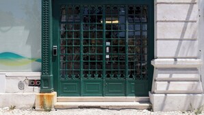 A green metal gate with a number 76 above it, leading to a building with a white stone facade.