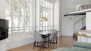 A modern living room with a dining area, large windows, and a staircase.