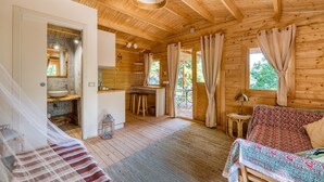 Interior de una cabaña de madera con cama, sofá, zona de comedor y baño.