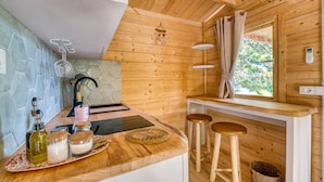 Interior de madera con una encimera de cocina, taburetes, una ventana con cortinas y una pared de piedra.
