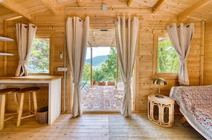 A wooden cabin with a bed, a desk, and a view of the outdoors.