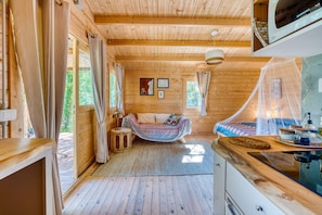 A wooden cabin interior with a bed, a dining area, and a kitchen.