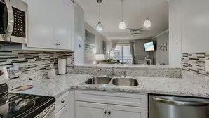 A modern kitchen with white cabinets, a double sink, a stove, and pendant lights.