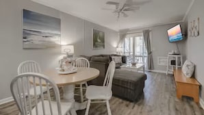A modern living room with a dining area, a ceiling fan, and a TV mounted on the wall.