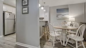 A modern kitchen with white cabinetry, a stainless steel refrigerator, and a dining area with a round table and white chairs.