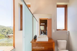 Une salle de bain moderne avec un meuble-lavabo en bois, un grand miroir et une vue sur l’extérieur.