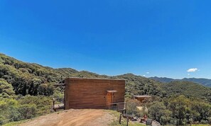 A wooden cabin with a dirt path leading to it, surrounded by lush greenery and mountains in the background. - Cabana de Luxo na Serra Catarinense Vst018 (Anitapolis)
