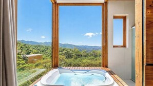 A hot tub on a wooden deck with a view of mountains and greenery.