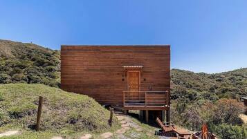 A wooden cabin with a door and a bench outside, surrounded by a natural landscape.